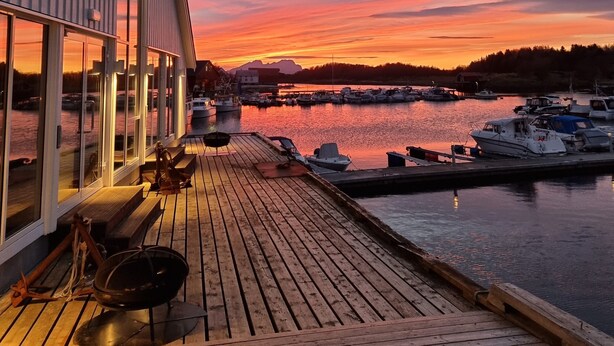 Una terraza de madera con vistas a un puerto deportivo y barcos al atardecer.