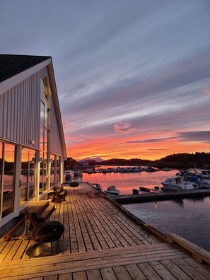 A wooden deck with a view of a marina and boats during sunset. - Kjerringøy Bryggehotell (Bodo)