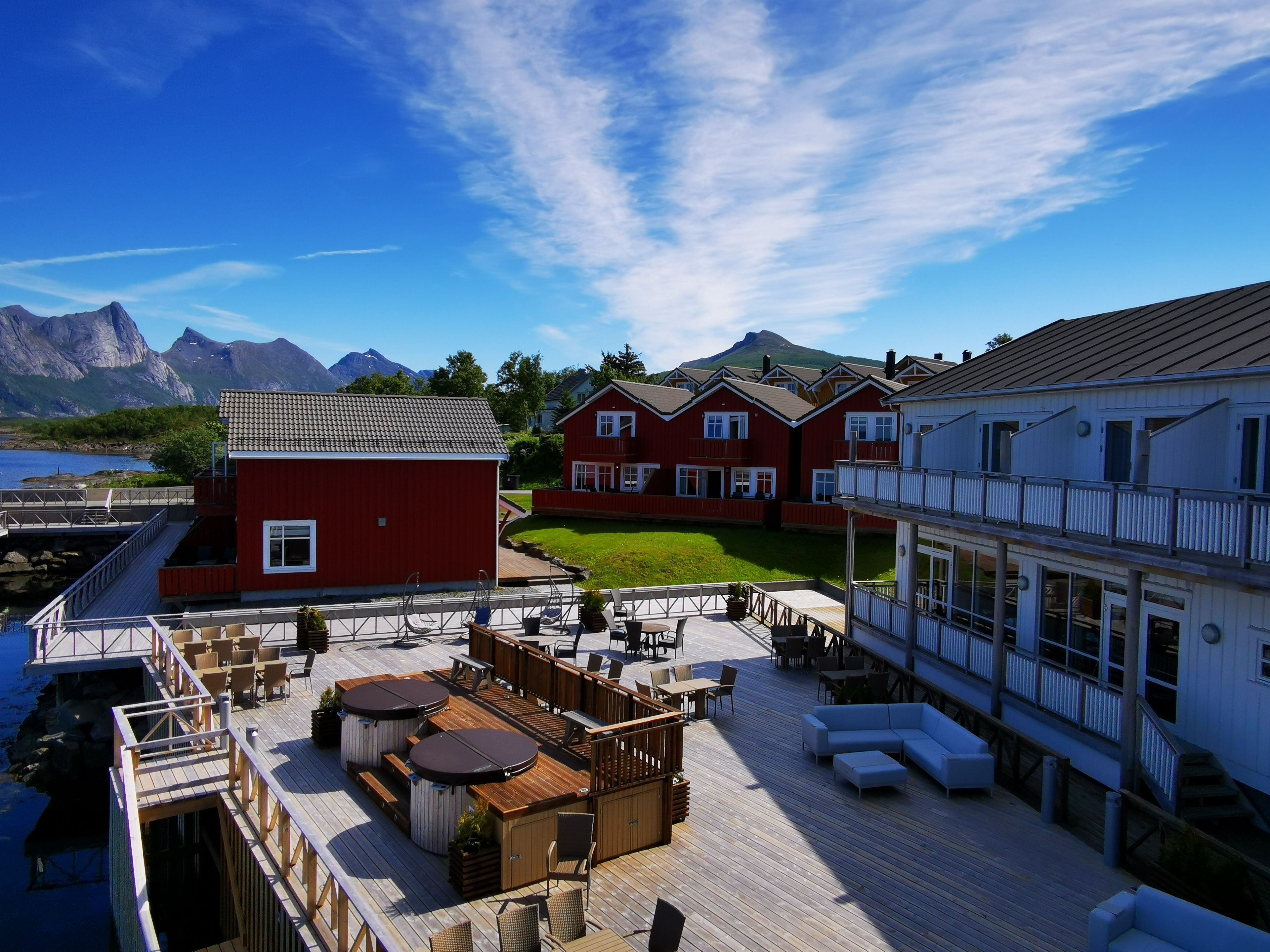A wooden deck with outdoor seating, a red building, and a mountain view.