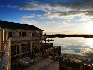 A waterfront building with a deck, outdoor seating, and a view of the water. - Kjerringøy Bryggehotell (Bodo)