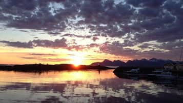 A sunset over a calm body of water with mountains in the background and a row of cabins along the shore.