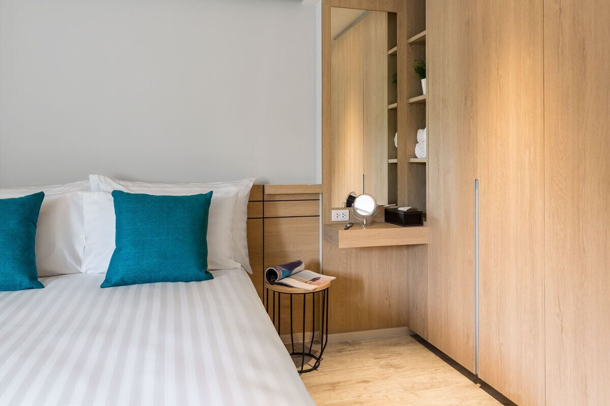 A bedroom with a bed, a small table with a magazine, a mirror, and a wooden wardrobe.