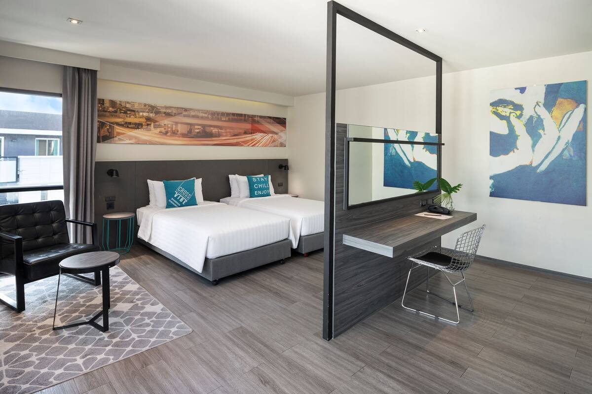 Ein modernes Hotelzimmer mit einem Bett, einem Schreibtisch, einem Sessel, einem kleinen Tisch und einem großen Spiegel.