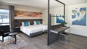 A modern hotel room with a bed, a desk, a chair, a small table, and a large mirror.