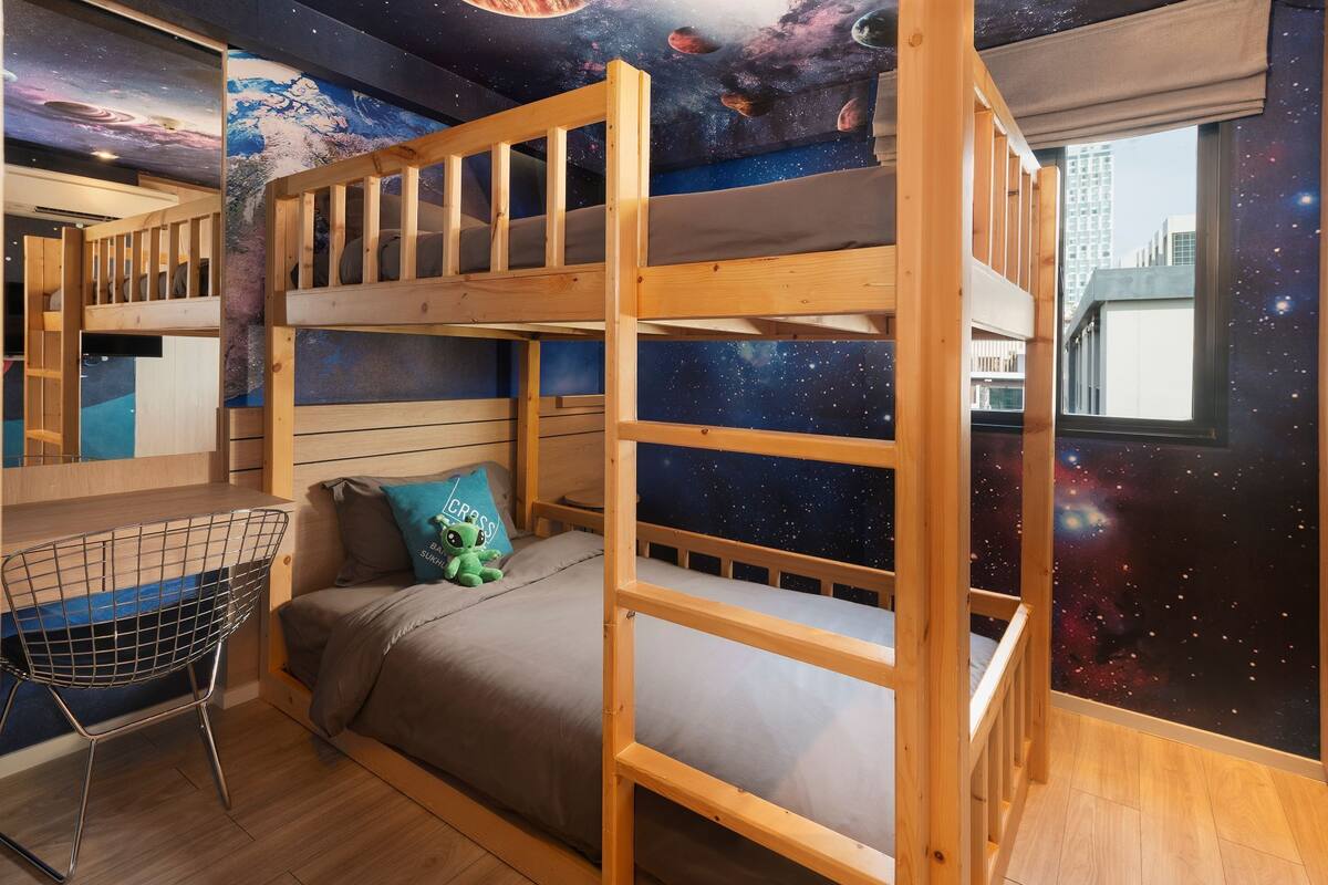 Ein Schlafraum mit Etagenbett, Wandgemälde zum Thema Galaxie, Schreibtisch und Stuhl.