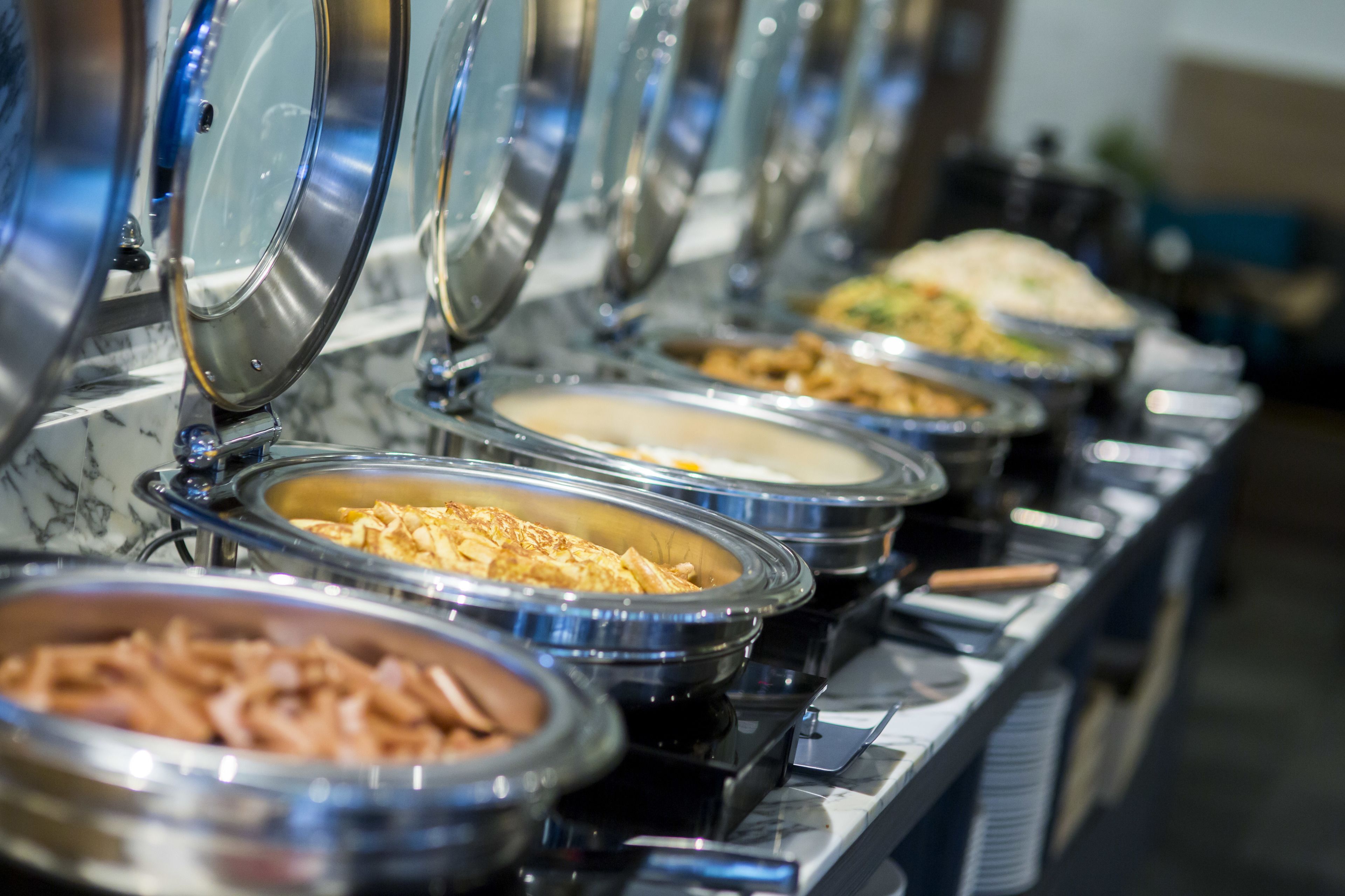 Buffet com diversos pratos em recipientes de metal.