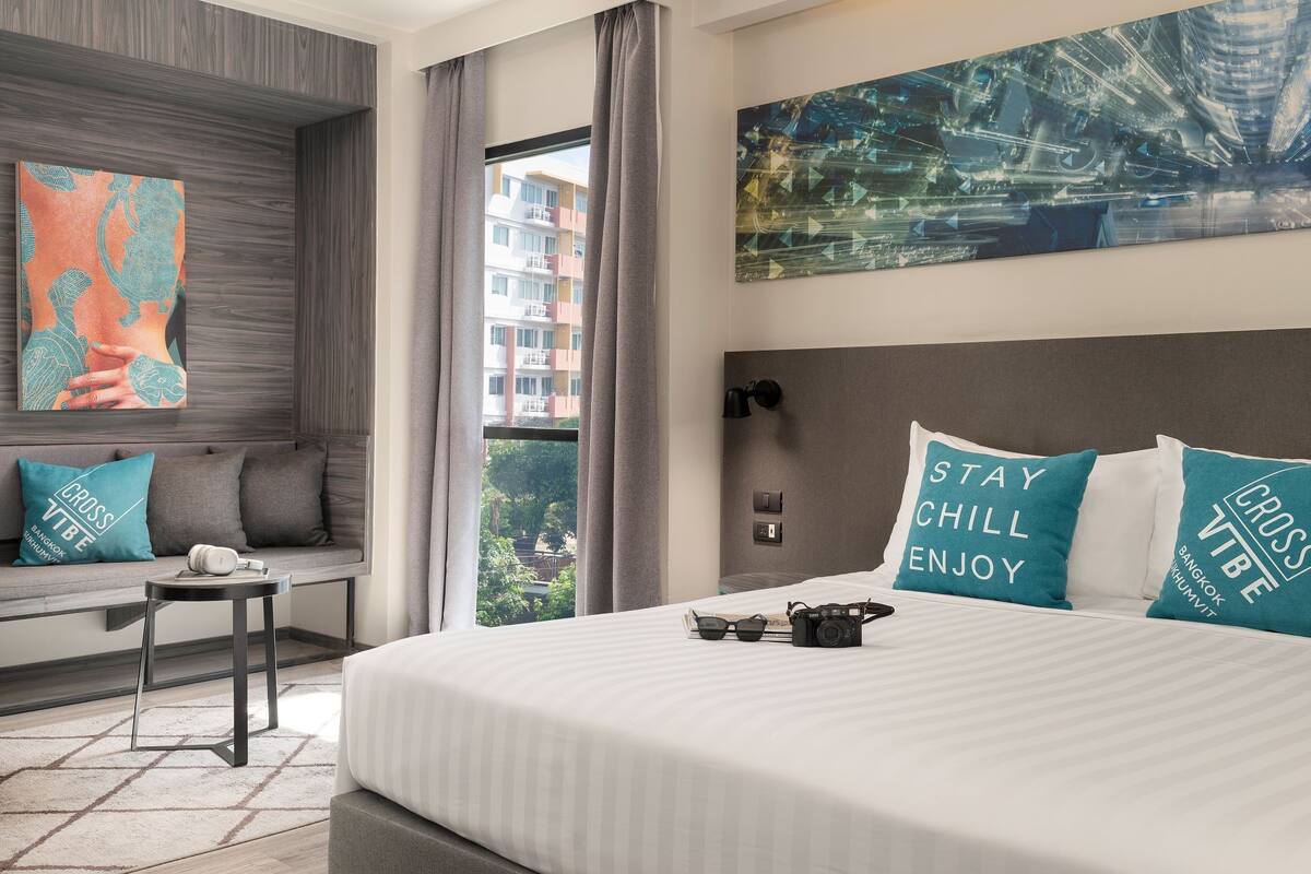 Ein Hotelzimmer mit einem großen Bett, einer Couch, einem kleinen Tisch und Blick auf Gebäude durch ein Fenster.