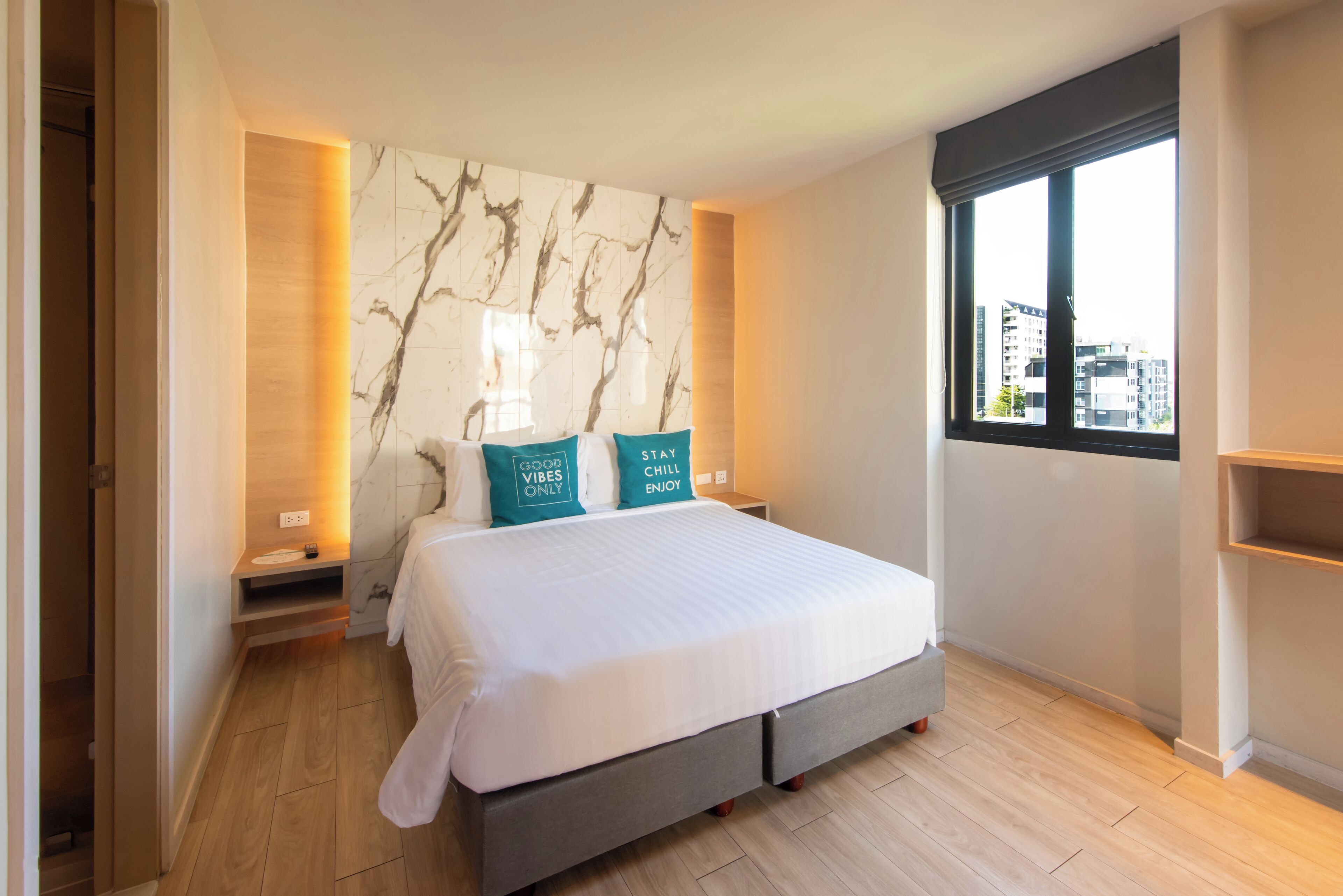 A modern bedroom with a marble headboard, a large bed with two pillows, a bedside table, and a window with a city view.