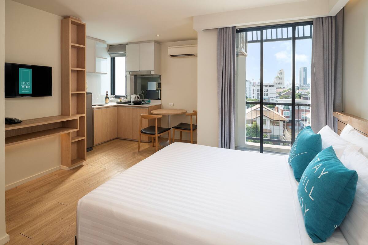 Ein Hotelzimmer mit Bett, Fernseher, einer Küchenzeile und einem Balkon mit Blick auf die Stadt.