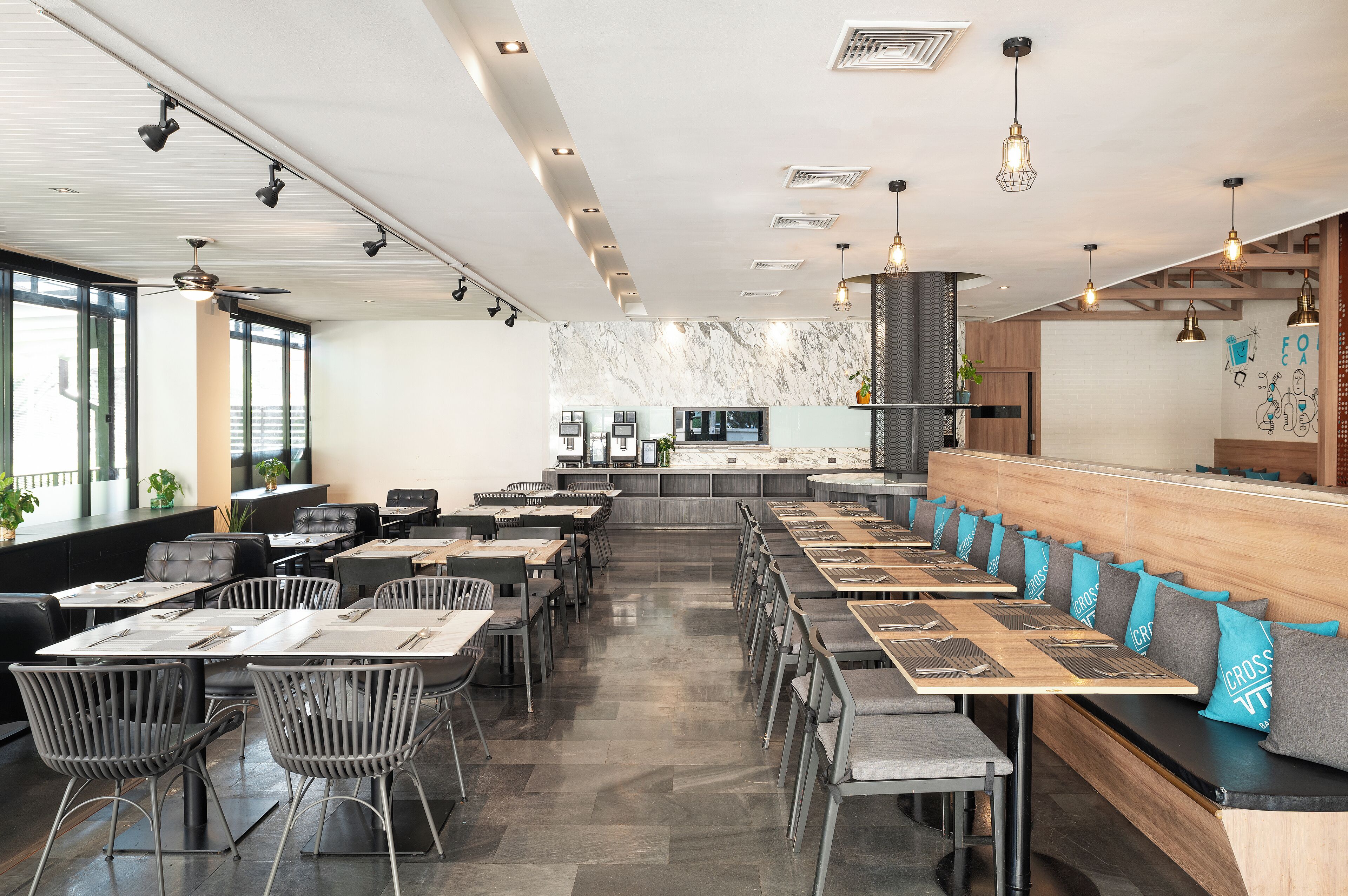 A modern restaurant with a long counter, multiple tables, and chairs.