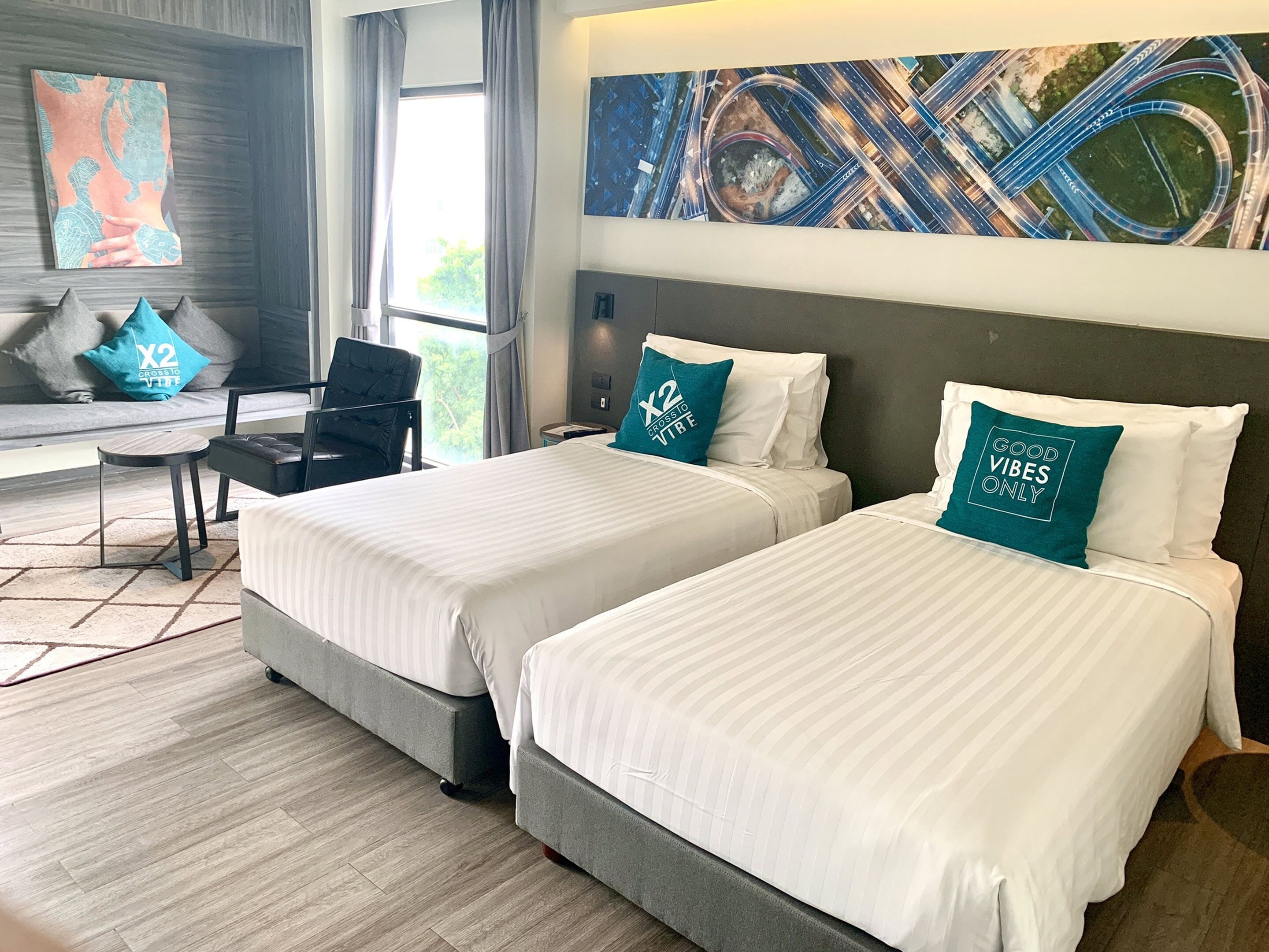 Une chambre d’hôtel avec deux lits, un bureau, une chaise et des œuvres d’art accrochées aux murs.