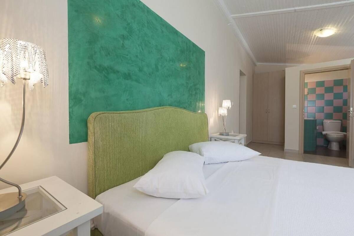 A hotel room with a green accent wall, a bed with white bedding, a bedside table with a lamp, and a view of the bathroom.