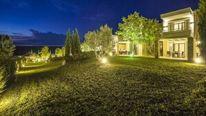 Ein modernes Hotel mit einem gut beleuchteten Garten und Meerblick bei Nacht.