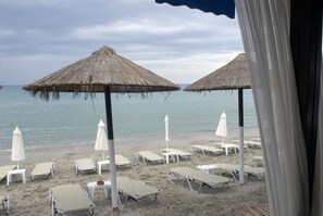 Ranta, jossa on aurinkotuoleja ja olkikattoisia aurinkovarjoja.