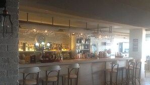 Una zona de bar con pared de ladrillo, taburetes y una variedad de botellas y vasos en estanterías.