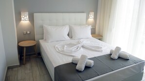 Una cama bien tendida con sábanas y toallas blancas, dos mesitas de noche y un cabecero moderno.