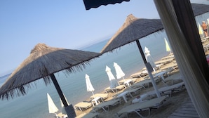 Una playa con tumbonas y sombrillas de paja.