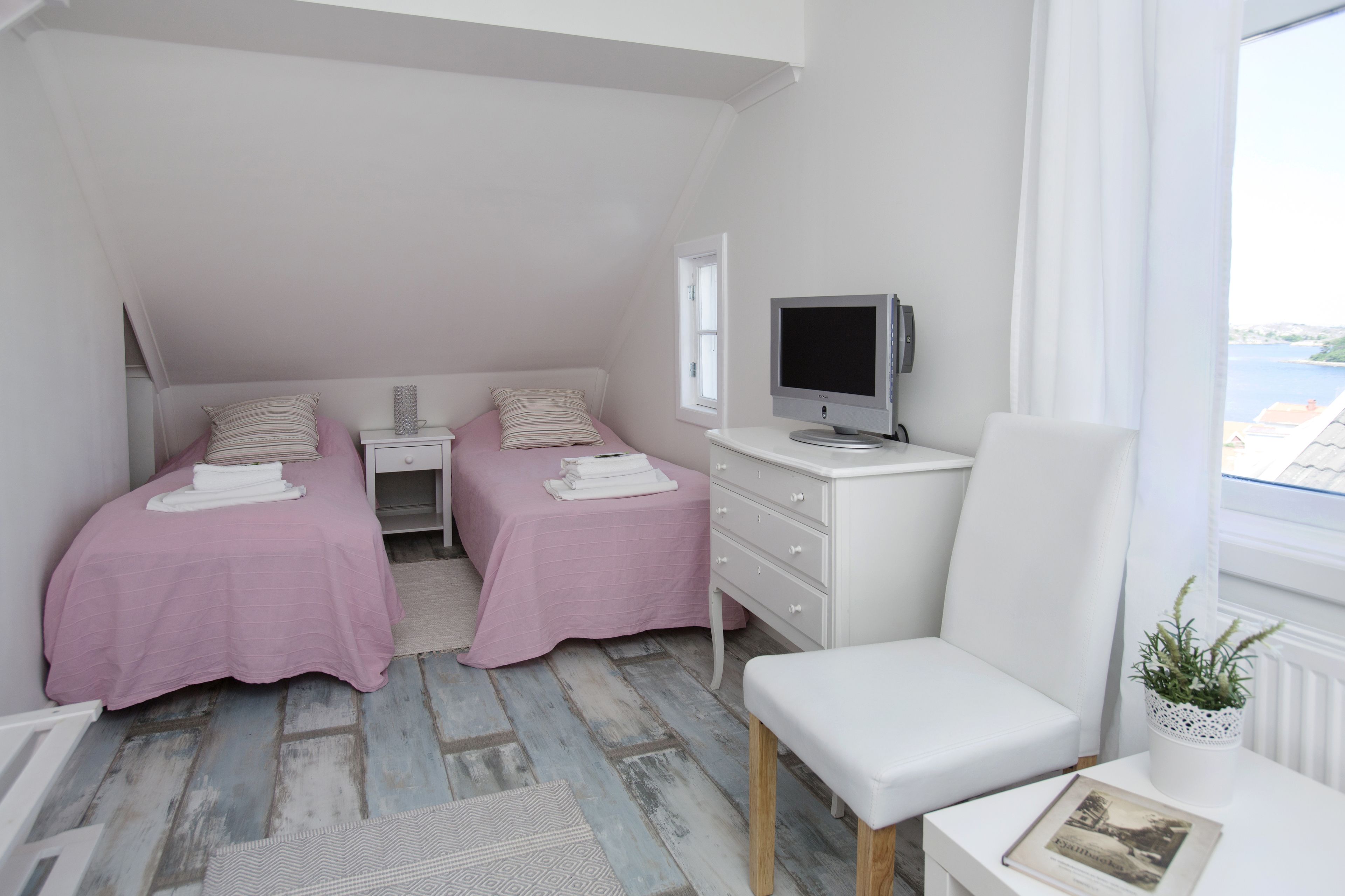 A bedroom with two beds, a desk, a chair, a TV, and a window with a view.