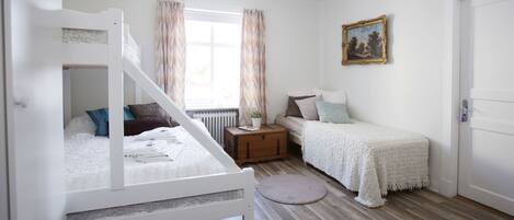 A bedroom with a bunk bed, a single bed, a chest of drawers, a round rug, and a painting on the wall.