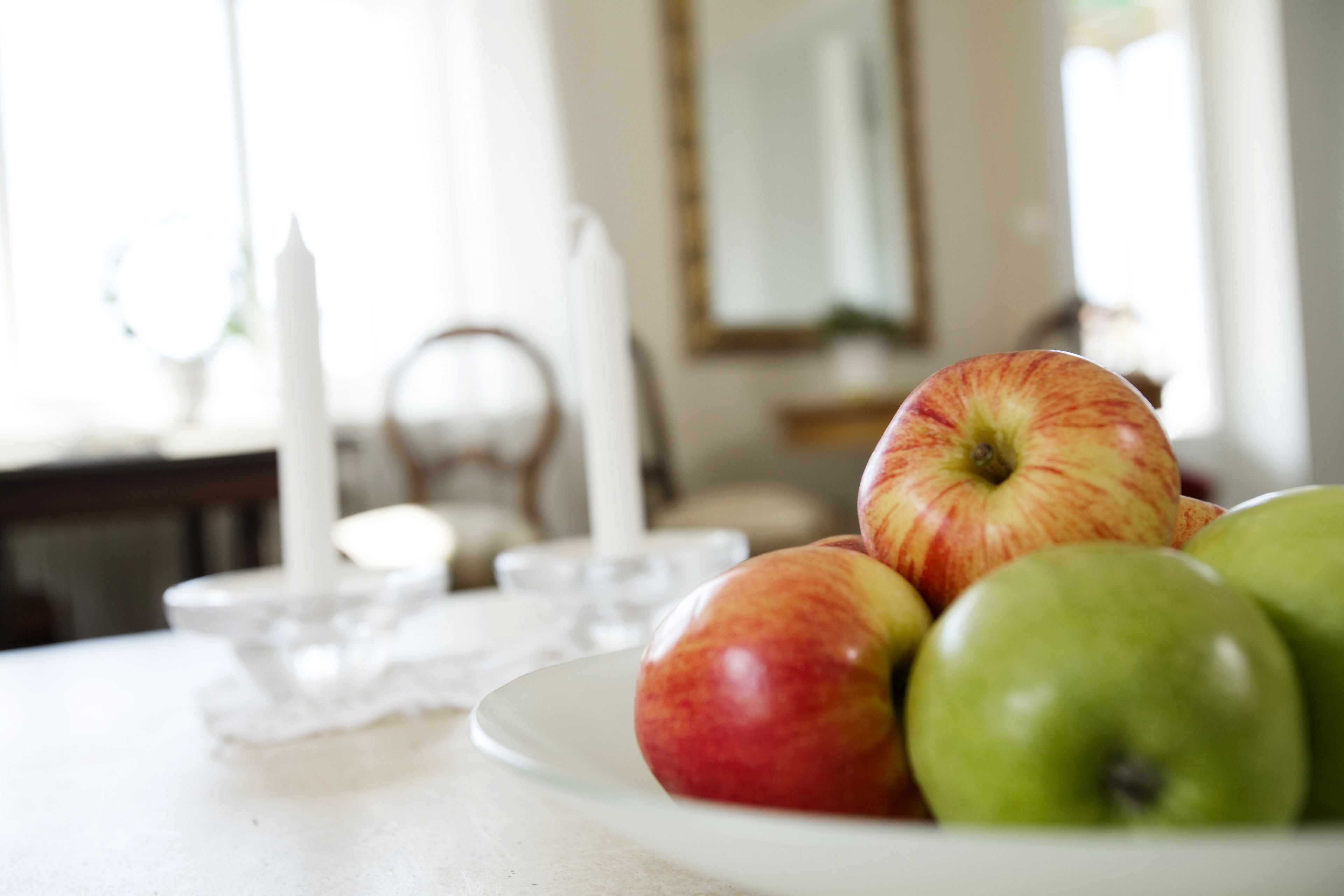 A plate of apples on a table with a candle and a mirror in the background.