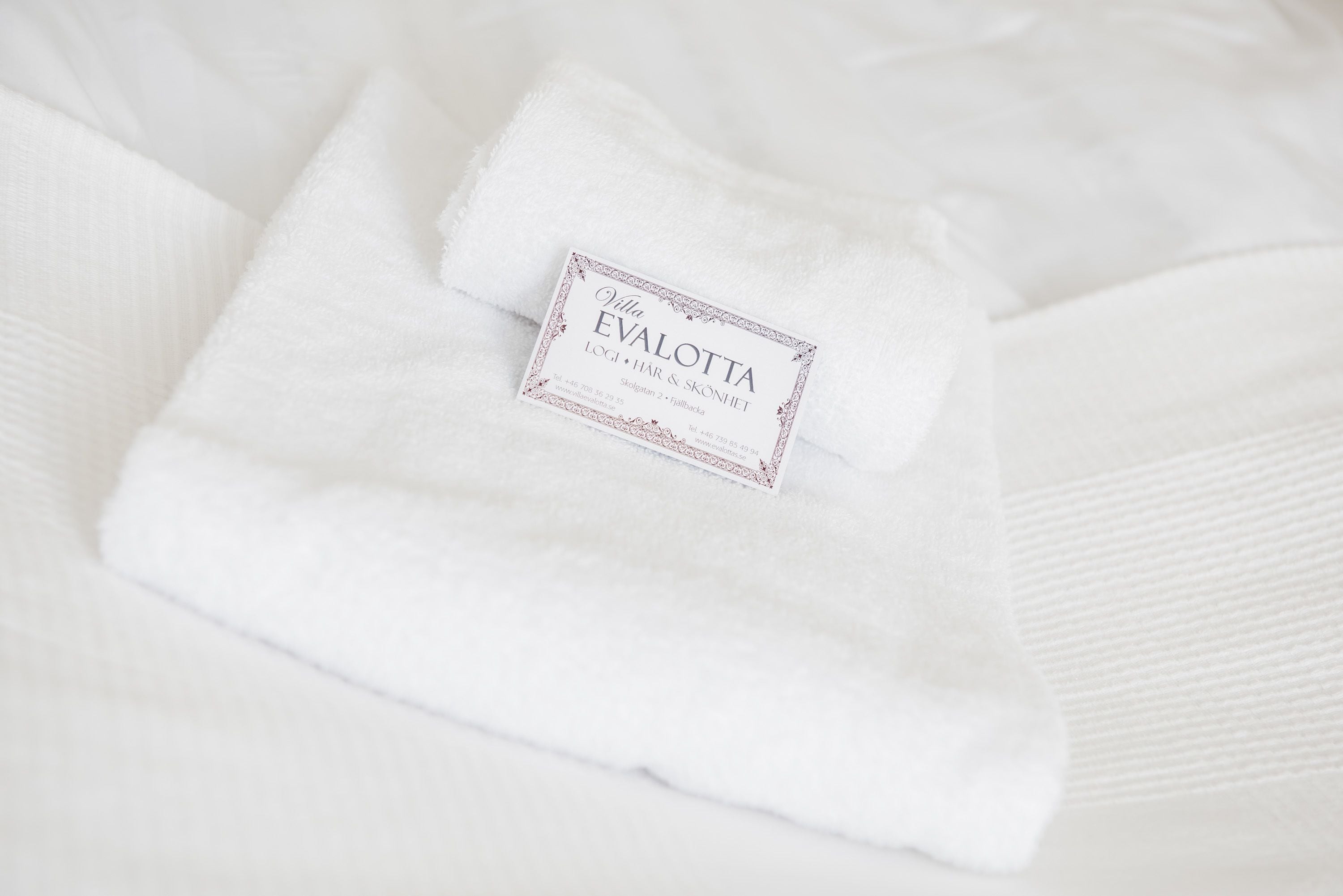 A neatly folded white towel with a label that reads "Villa EVALOTTA LUGI - HAR & SKONIET."