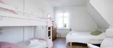 Ett sovrum med en våningssäng, en enkelsäng, en stol, en byrå och ett fönster med gardiner.