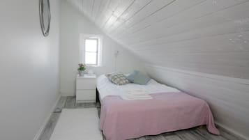 A bedroom with a sloped ceiling, a bed with a pink bedspread, a nightstand with a plant, and a window.