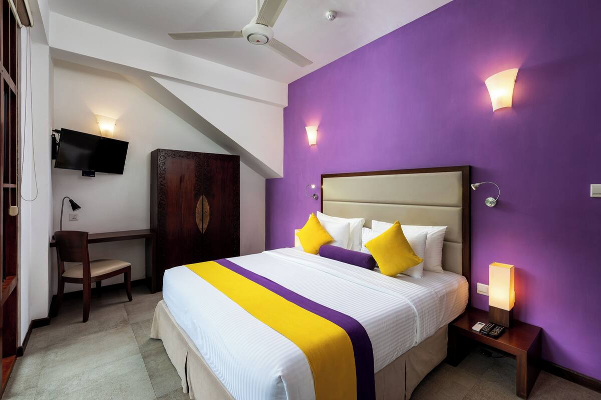A bedroom with a bed, a desk, a chair, a TV, and a ceiling fan.