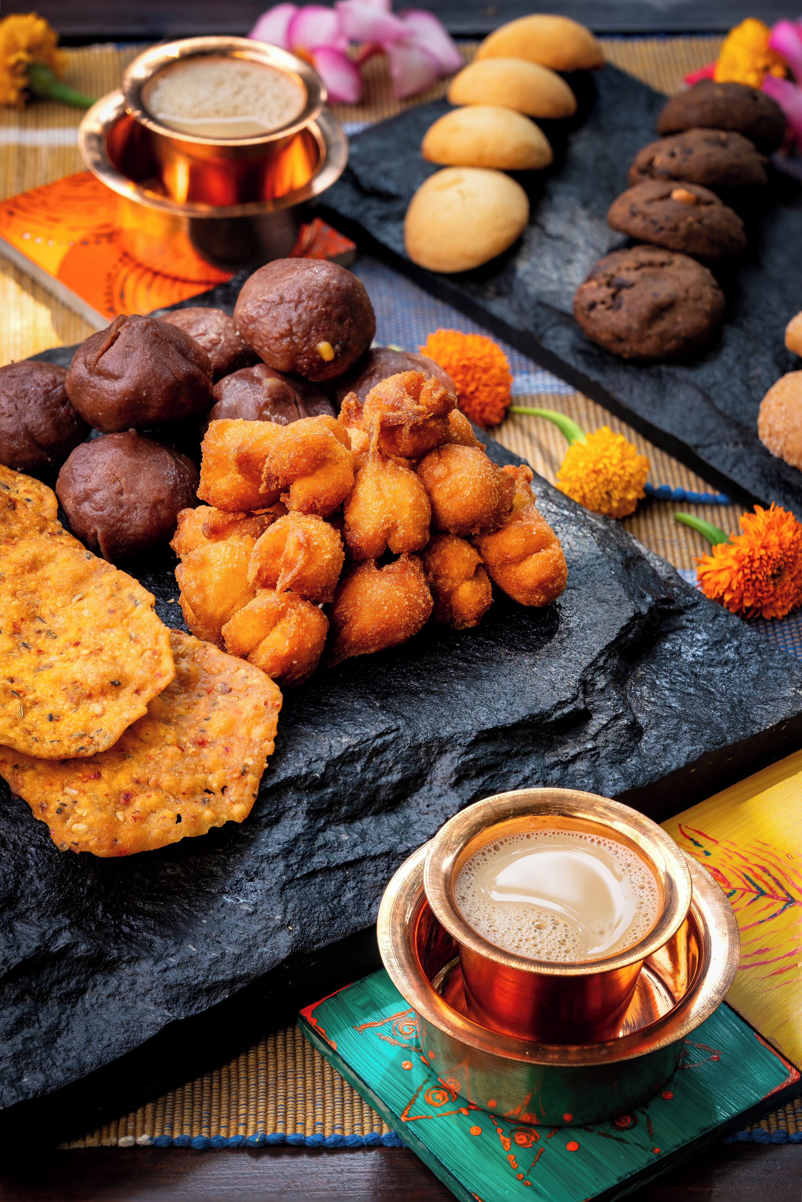 A variety of Indian snacks and beverages on a slate board.