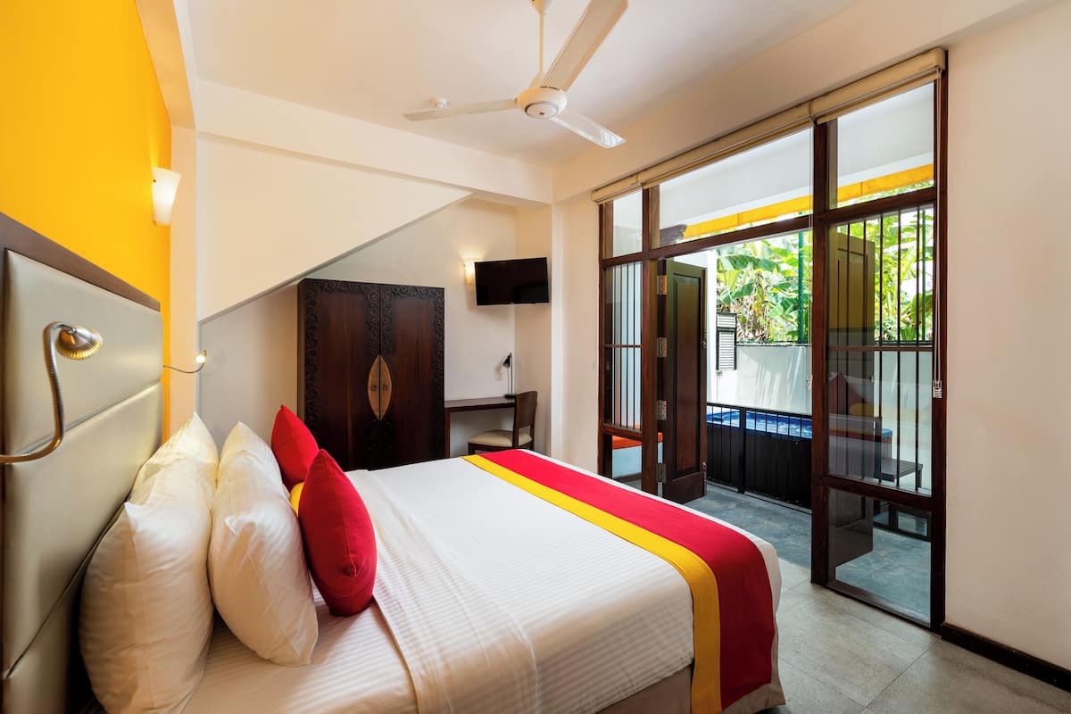 A hotel room with a bed, a ceiling fan, a TV, and a sliding glass door to the outside.