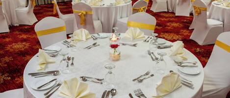 A banquet hall with round tables set for a formal event, each with white tablecloths, silverware, and yellow sashes on chairs.