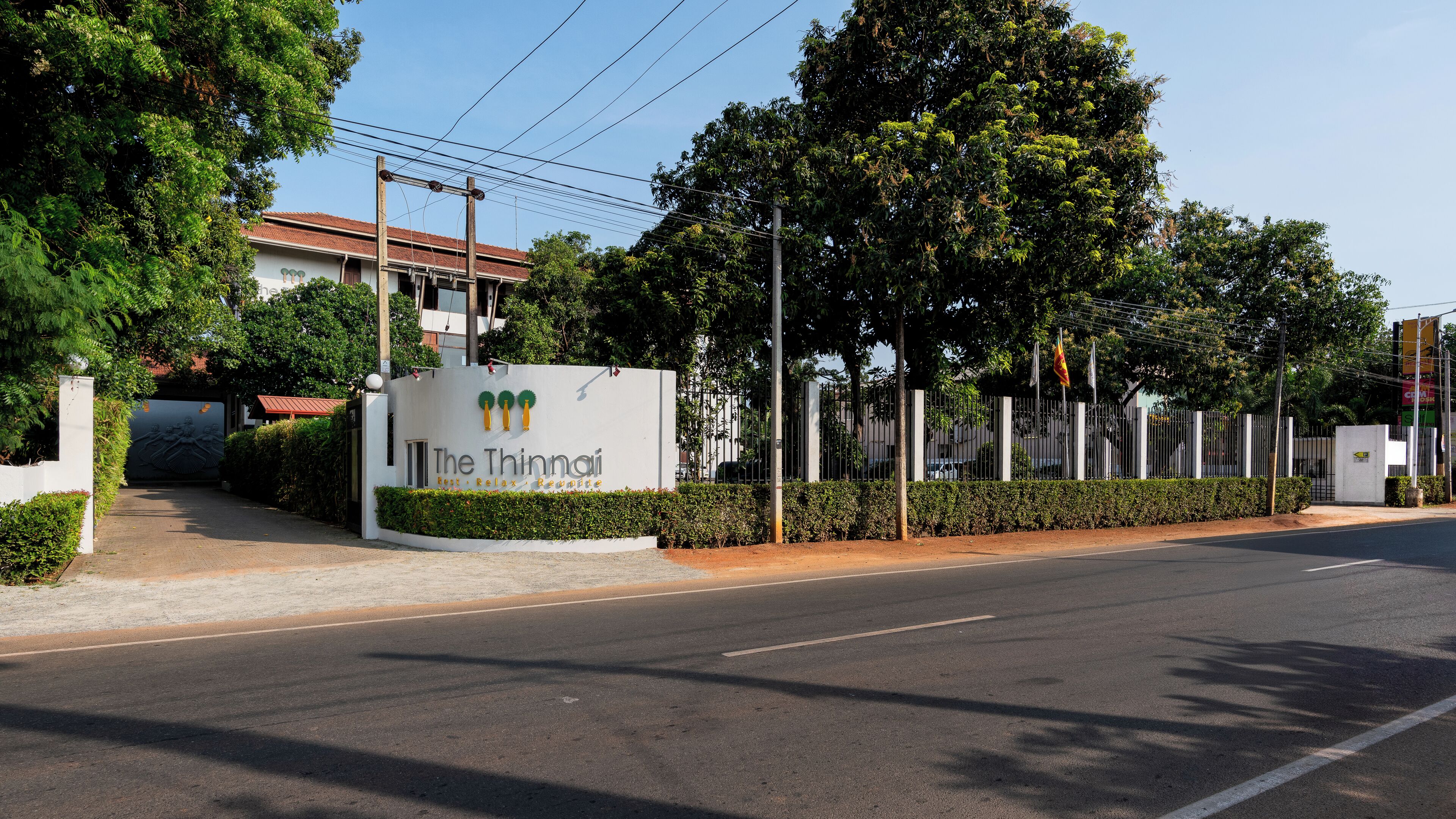 A gated entrance with a sign for 'The Thinning' hotel, surrounded by greenery and a clear sky.