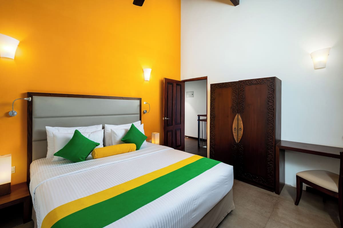 A hotel room with a bed, bedside lamps, a wooden wardrobe, and a desk.