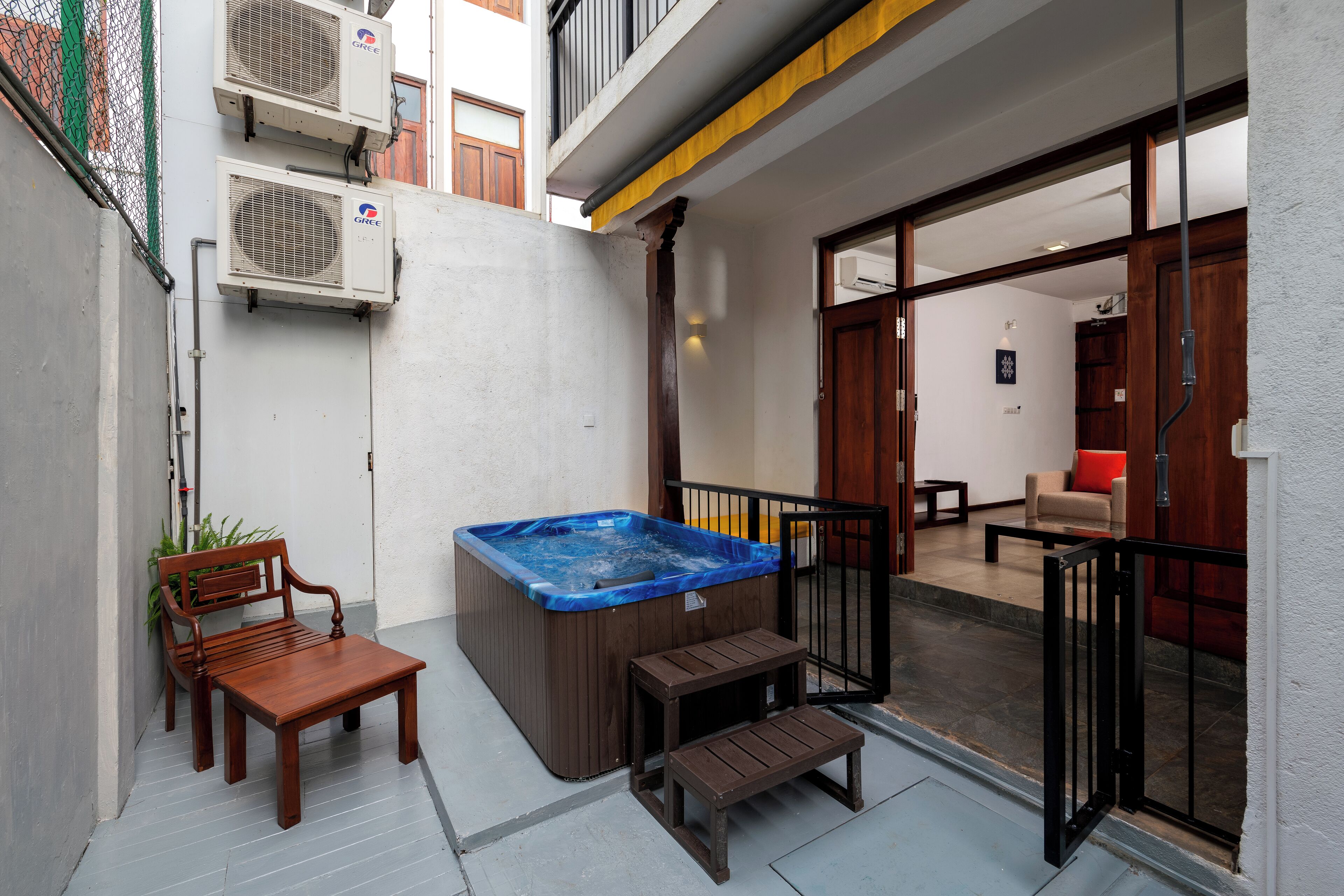 A hot tub, wooden bench, and a small table in a courtyard with a view of the interior.