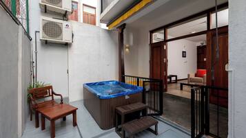 A hot tub, wooden bench, and a small table in a courtyard with a view of the interior.