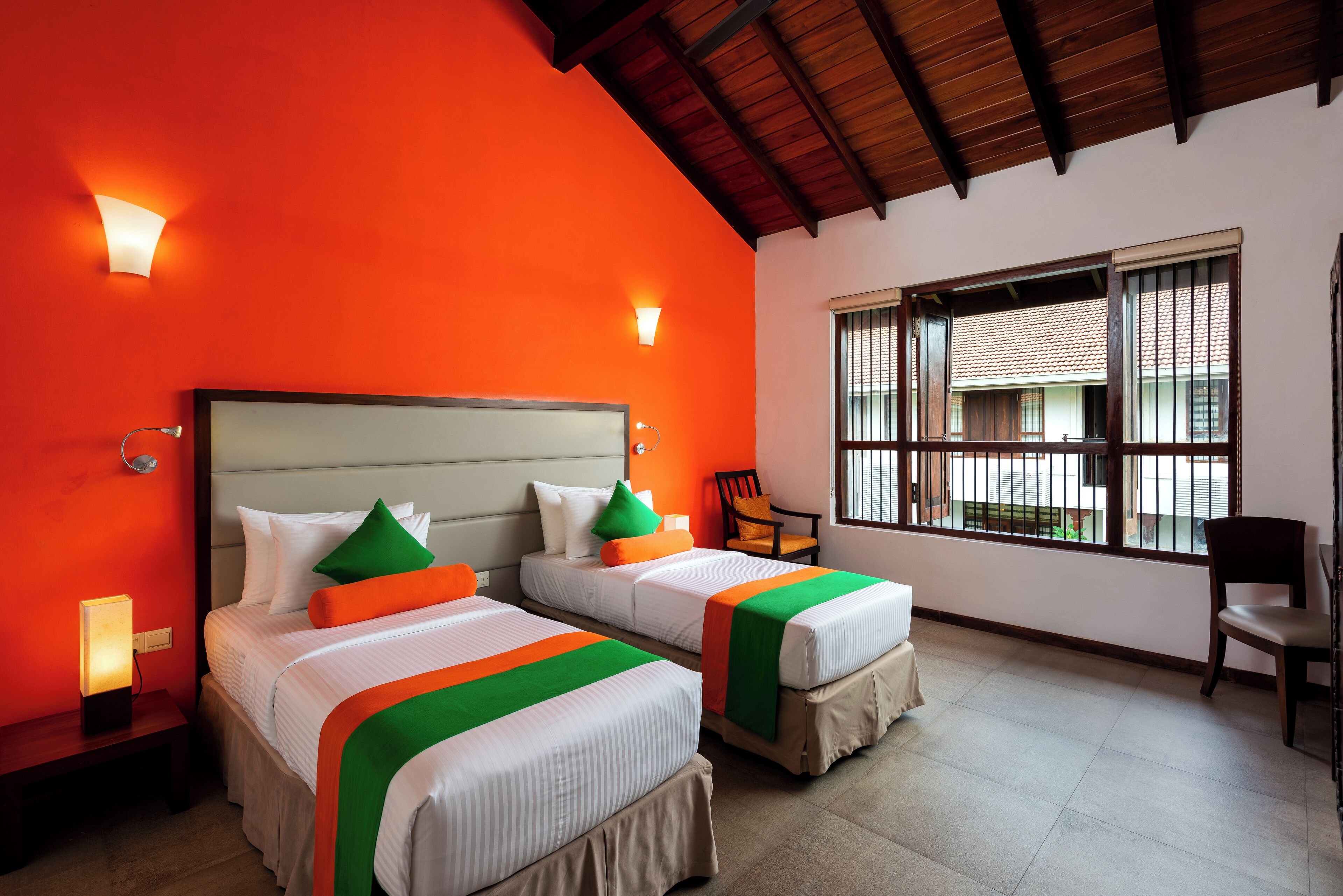 A hotel room with two beds, a wooden ceiling, a window with blinds, and a chair.