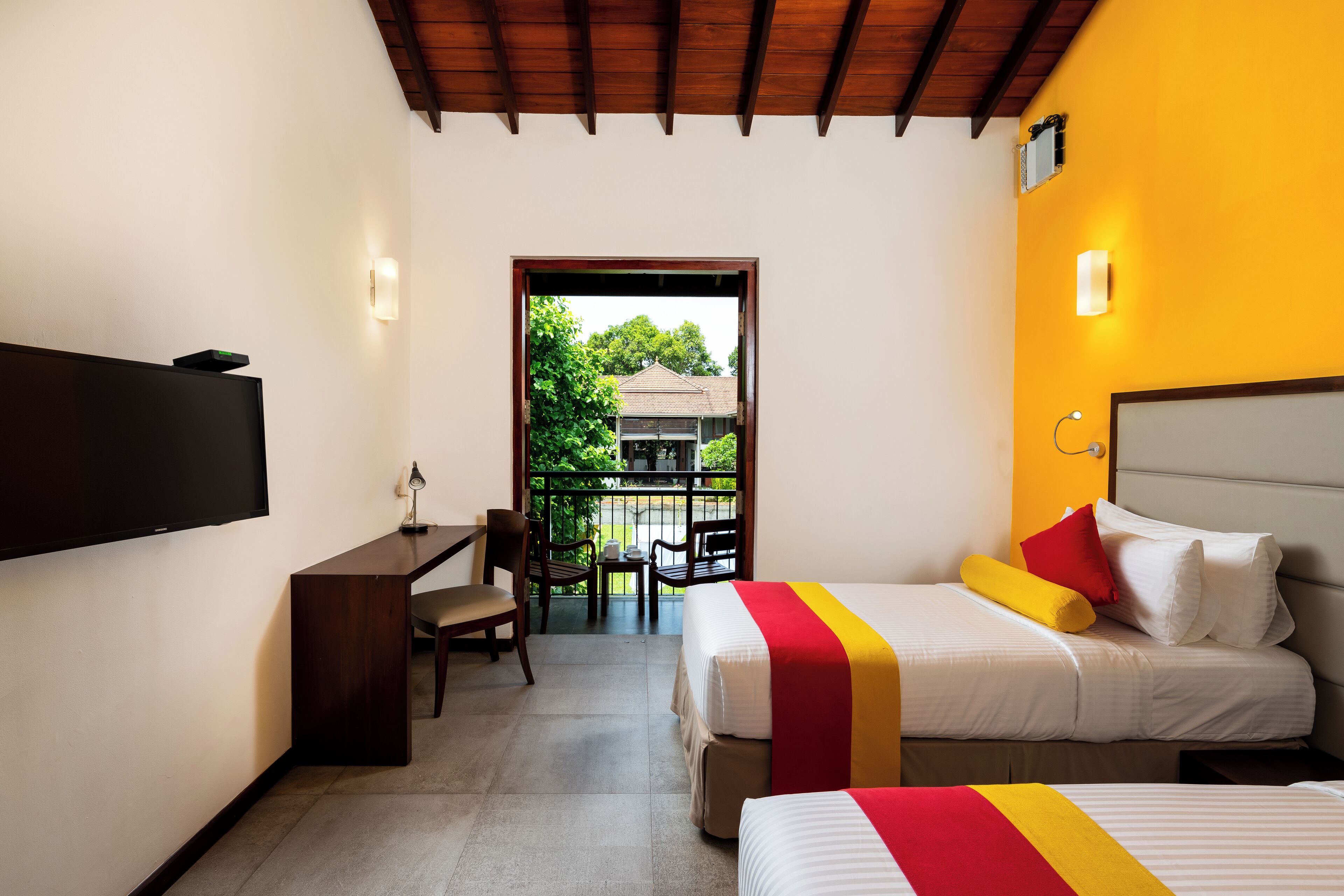 Habitación de hotel con dos camas, un escritorio y televisión. Tiene un balcón con vistas a zonas verdes.