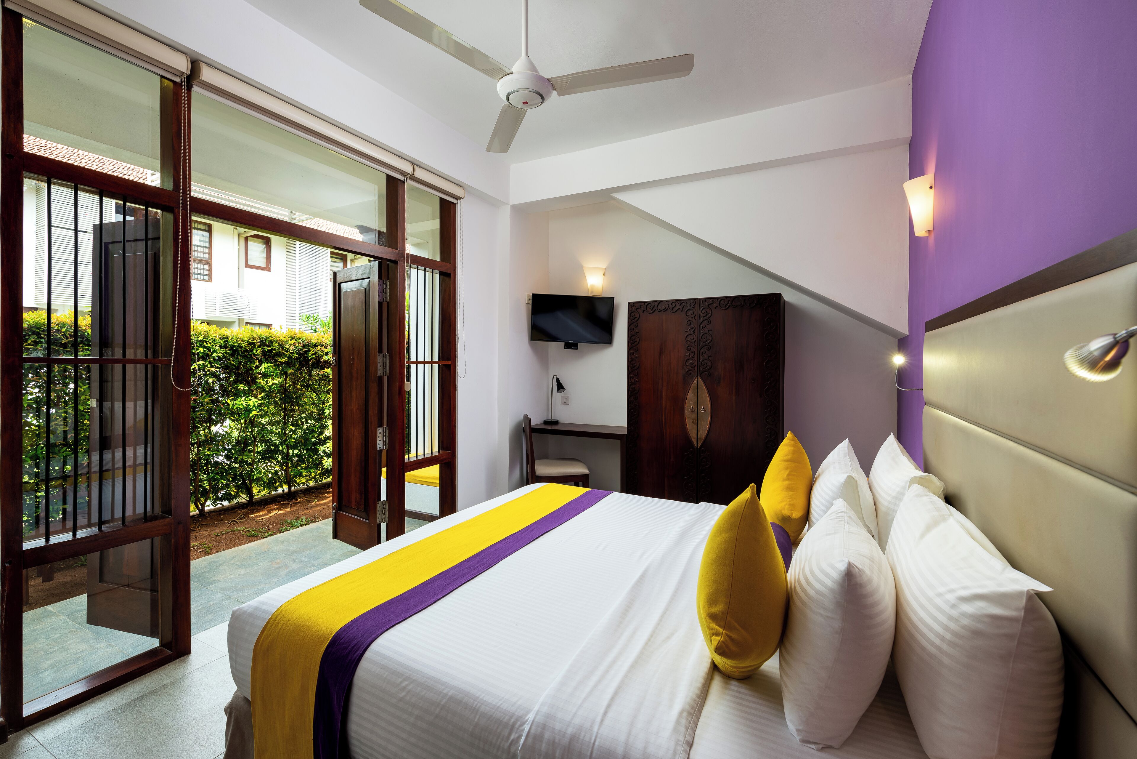A hotel room with a bed, a TV, a desk, and a view of the outside.