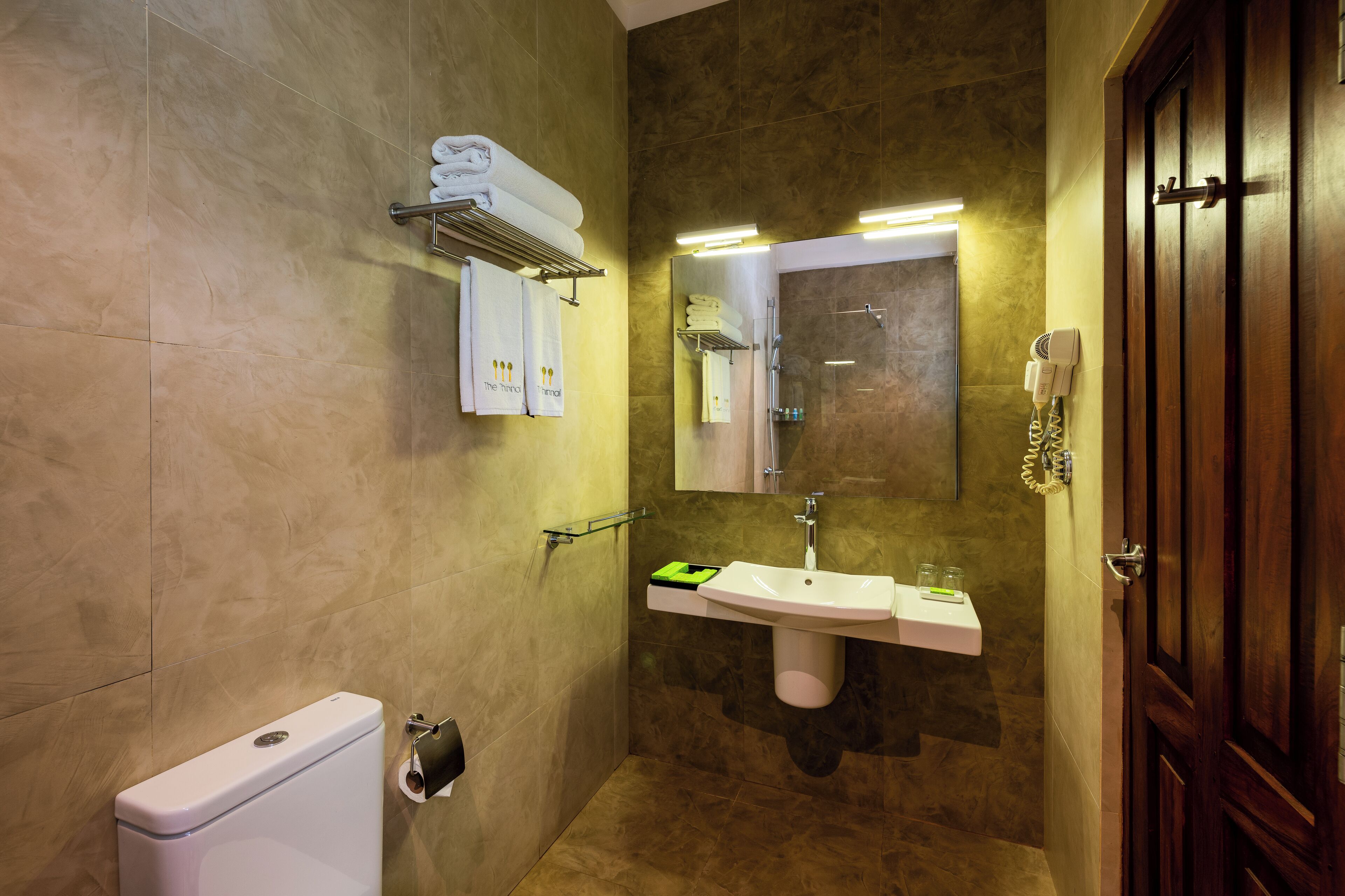 A bathroom with a toilet, sink, and mirror. There are towels on a rack and a hairdryer on the wall.