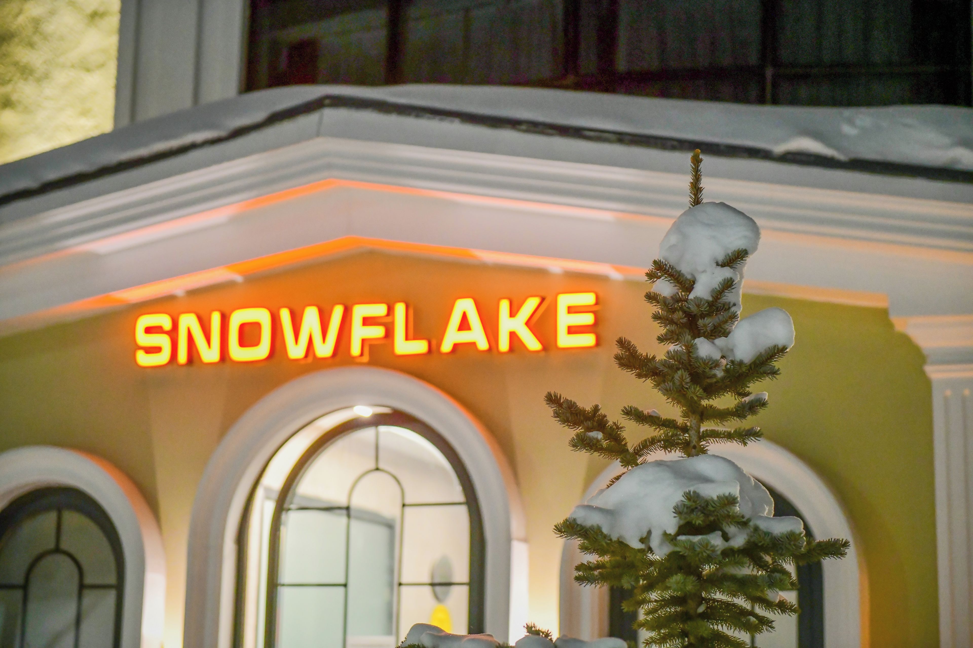 Un edificio con un letrero de neón que dice 'SNOWFLAKE' y un árbol cubierto de nieve al frente.