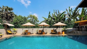 A swimming pool with sun loungers and umbrellas, surrounded by lush greenery. - The Thinnai Hotel (Jaffna)