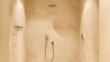 Ein modernes Duschbad mit beigen Fliesen, einer Handbrause und einer an der Wand montierten Duschbrause.