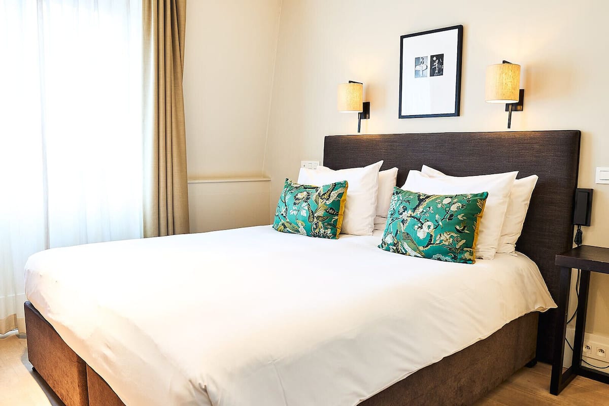 A hotel room with a large bed, two wall-mounted lamps, and a framed picture on the wall.