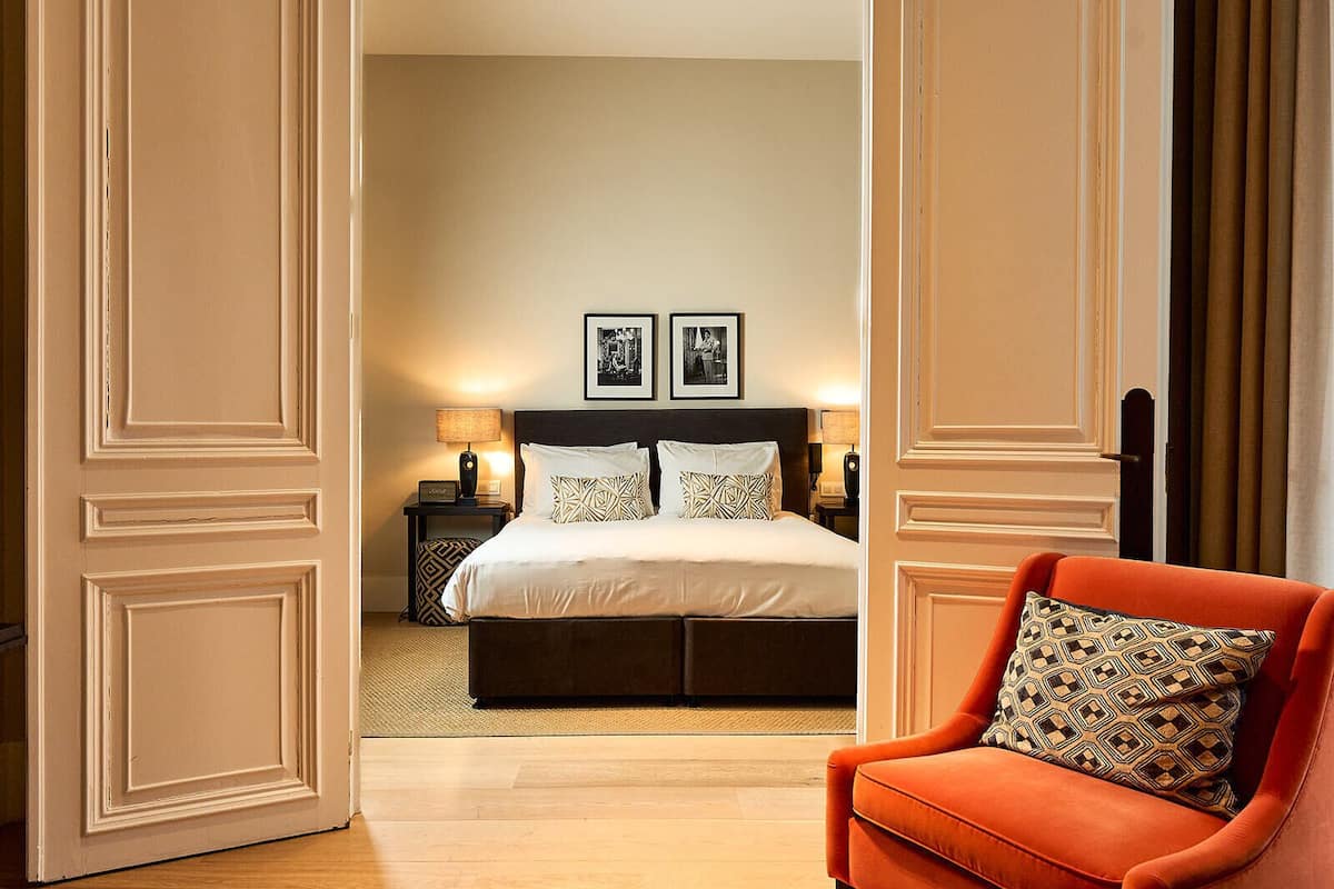 A hotel room with a bed, bedside tables, a lamp, and a chair.