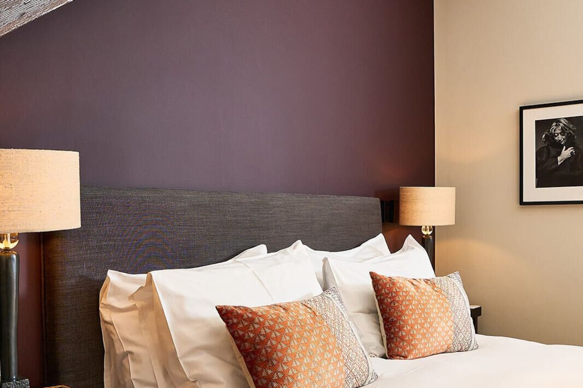 A hotel room with a large bed, two bedside lamps, a framed picture on the wall, and a wooden ceiling beam.