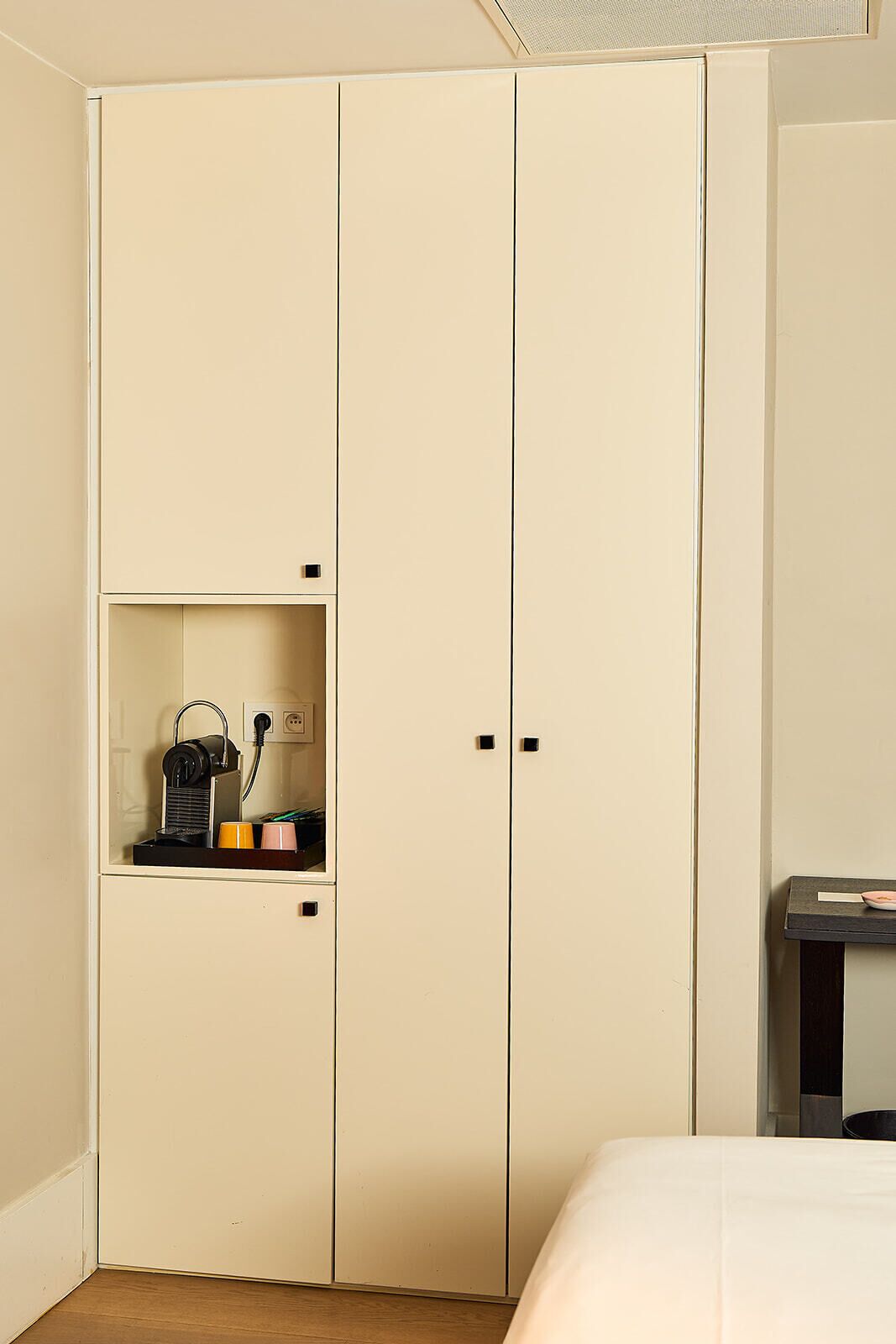 A beige wardrobe with a shelf containing a kettle, cups, and a power outlet.