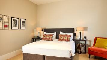 Une chambre d’hôtel bien aménagée, avec un grand lit, deux tables de chevet dotées de lampes, une chaise et un tableau d’affichage mural orné de photos encadrées.
