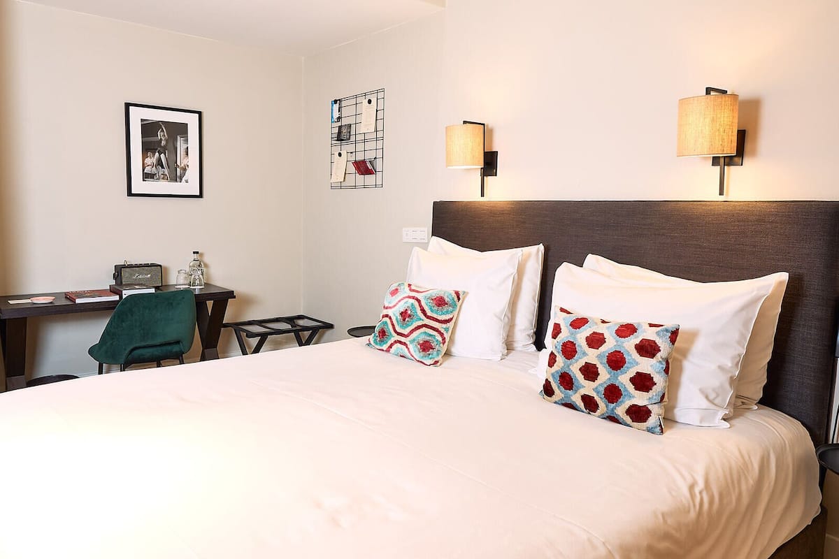 A hotel room with a large bed, two bedside lamps, a desk with a chair, and a wall with framed pictures.