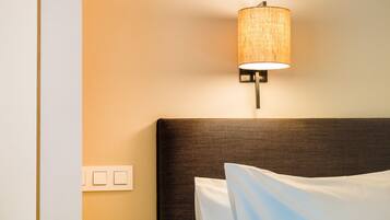Quarto de hotel com cabeceira, luminária fixada na parede e tomada.