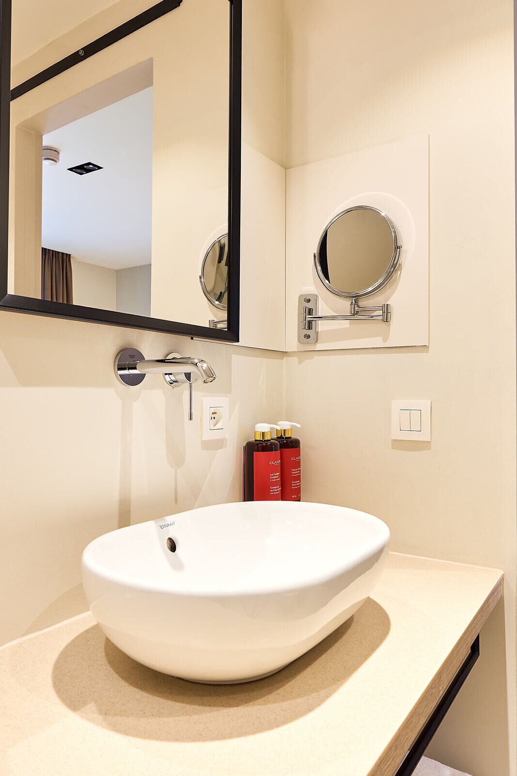 A bathroom with a white sink, two round mirrors, and a bottle of Clairol shampoo.